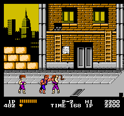 Double Dragon: Billy and Jimmy walk down a city street past an orange brick building, with the skyline behind them