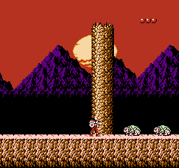 Rygar: the warrior stands before a tall stone pillar at sunset, with two armored crawlers approaching